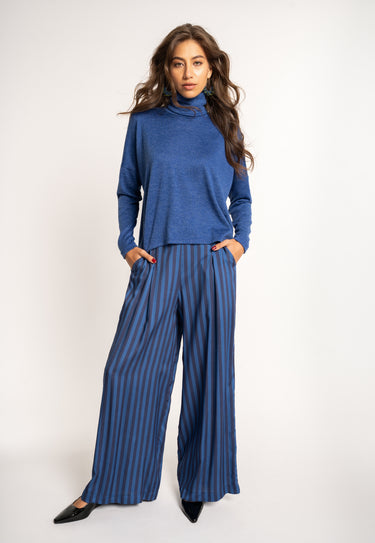 Woman wearing a blue turtleneck and striped pants on a white background
