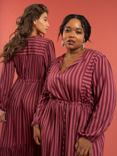 Two women wearing matching maroon and white striped dresses against a red background