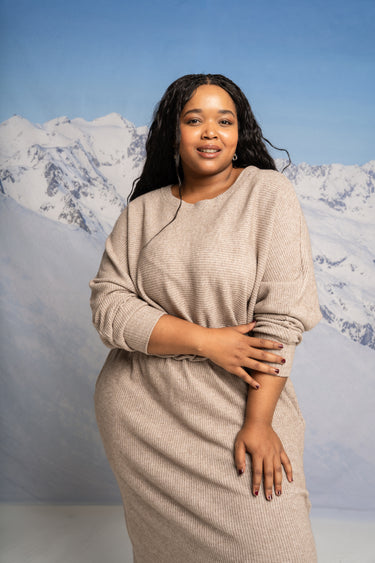 Woman in a beige dress standing against a mountainous background