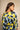 A woman shown from the back wearing a loose-fitting kaftan dress with a bold abstract pattern in yellow, light blue, and black, set against a neutral beige background.