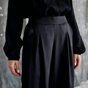 Person wearing a black outfit with wide-leg pants against a neutral background