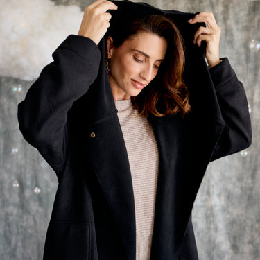 Woman wearing a black coat over a beige outfit against a neutral background