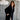 Woman wearing a black coat standing against a textured gray wall with decorative elements.