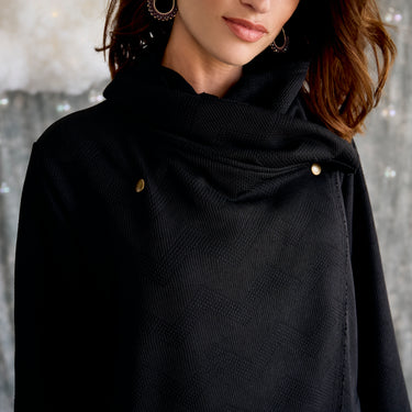 Close-up of a person wearing a black coat with gold buttons against a neutral background