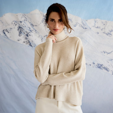 Woman wearing a beige sweater in front of a mountainous landscape