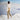 Person standing on a snowy mountain wearing a white lace top and beige pants.
