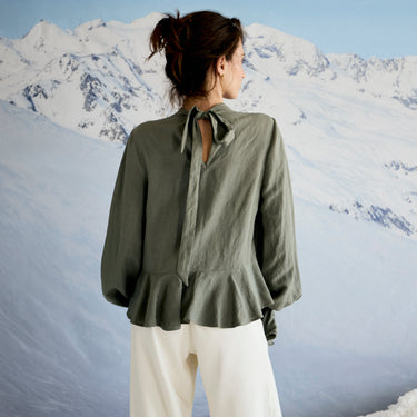 Person wearing a green blouse with a tie detail in a snowy mountain landscape