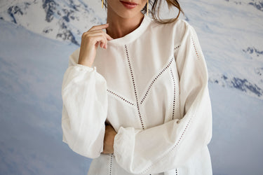 Woman wearing a white blouse with intricate patterns against a blurred background