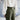 Person wearing a white blouse and olive green pants against a light blue wall.