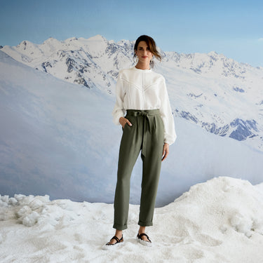 Person wearing a white top and green pants standing in a snowy landscape with mountains.