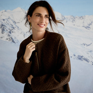 Woman wearing a brown jacket in front of a snowy mountain landscape