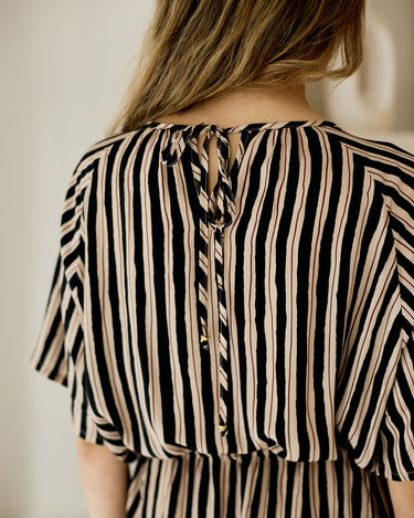 Close-up back view of a woman wearing a black and beige vertically striped dress with a tie-back neckline and short flutter sleeves.