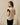 A woman wearing a color-blocked short-sleeve top with beige, white, and black panels, shown from the back in a minimalist indoor setting.