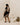 A woman wearing a black and beige floral tunic dress with striped hem and sleeves, walking down white steps in a minimalist studio setting.