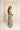 A woman modeling a long-sleeved maxi dress with a bold black and white abstract pattern, standing in front of a large beige canvas on a white studio floor.