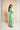 A woman wearing a long-sleeved maxi dress with a bold green and white abstract geometric pattern, standing in front of a beige backdrop.