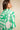 A woman shown from the back wearing a green and white abstract patterned blouse against a neutral beige background.