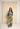 A woman modeling a matching two-piece jumpsuit set with a bold abstract pattern in yellow, navy, and light blue, standing in front of a large beige canvas backdrop.