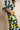 A woman wearing a loose, short-sleeve top and matching pants with a bold abstract geometric print in yellow, navy blue, and light blue, standing against a neutral beige textured wall.