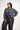 Woman wearing a colorful patterned blouse and dark pants on a white background
