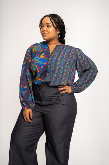 Woman wearing a colorful patterned blouse and dark pants on a white background