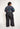 Person wearing a colorful patterned top and black pants on a white background