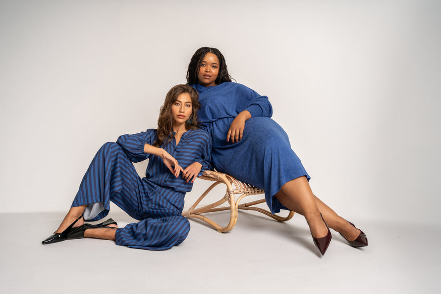 Two women in matching blue outfits sitting on a white background