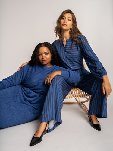 Two women wearing matching blue outfits sitting on a white background