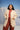 Woman wearing a beige coat over a red top and brown pants with a mountainous background