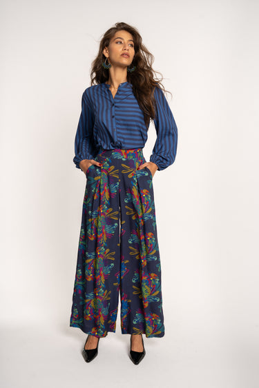 Woman wearing a blue striped shirt and colorful wide-leg pants on a white background