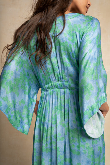 A woman wearing a blue and green tie-dye kaftan dress, shown from the back against a neutral beige background.