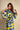 A woman wearing a loose dress with a bold abstract geometric pattern in yellow, black, and light blue-gray, posed against a warm beige textured backdrop.
