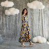 Woman in a patterned dress standing in front of a textured wall with cloud decorations.