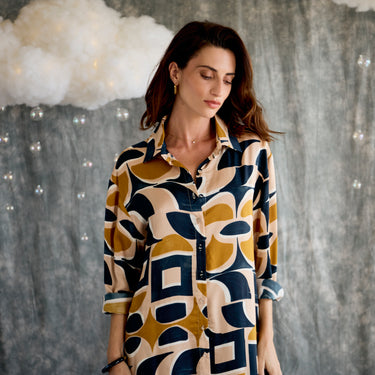 Woman wearing a patterned shirt against a textured wall.