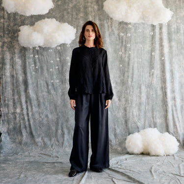 Woman in a black outfit standing against a textured gray wall with white cloud-like decorations.