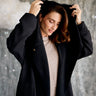 Woman wearing a black coat over a beige outfit against a neutral background