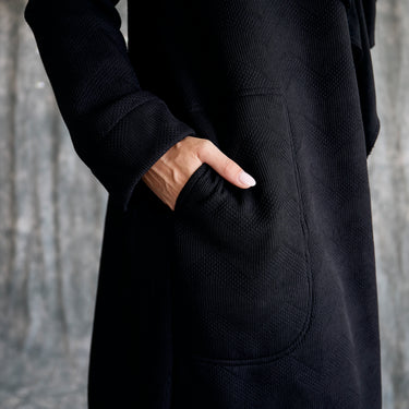 Person wearing a black textured coat with a neutral background