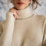 Close-up of a person wearing a beige turtleneck sweater with a blurred background