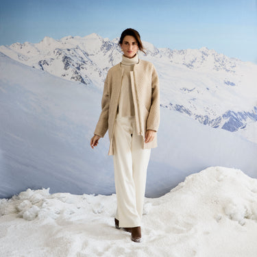 Person wearing a beige outfit standing in a snowy landscape with mountains.