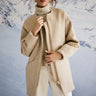 Person wearing a beige coat with a snowy mountain background