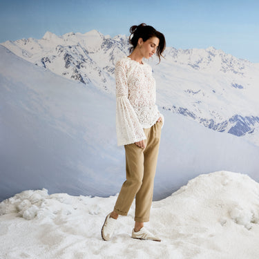Woman in a white lace sweater and beige pants standing on a snowy mountain