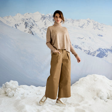 Person wearing a beige outfit standing in a snowy landscape with mountains in the background