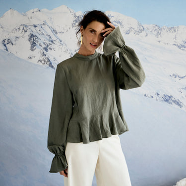 Woman wearing a green top and white pants against a mountainous background
