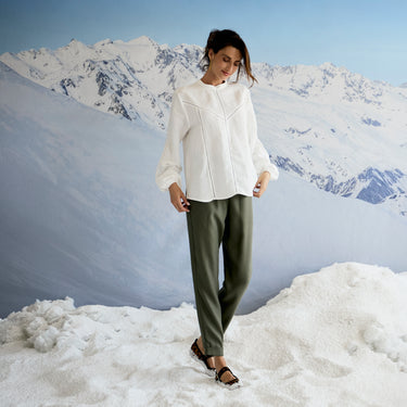 Person wearing a white shirt and green pants standing in a snowy landscape with mountains in the background