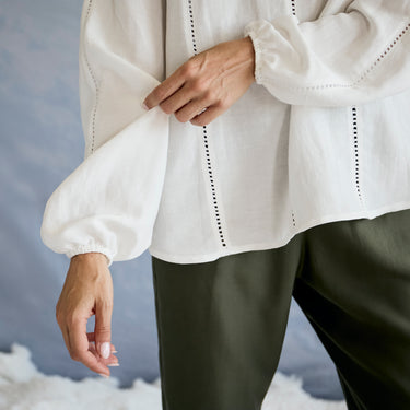 Close-up of a person wearing a white blouse with puffed sleeves against a blurred background