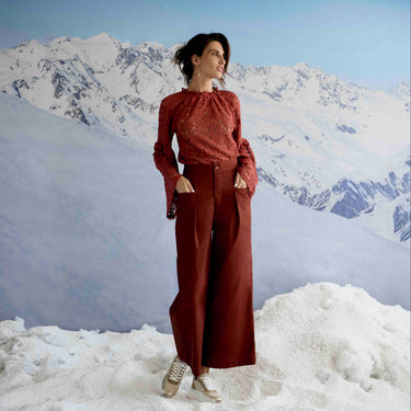 Woman in a red outfit standing in a snowy landscape with mountains in the background
