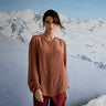 Woman in a brown blouse standing in front of snow-covered mountains
