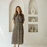 A woman modeling a short-sleeve midi dress with vertical black and beige stripes, standing in a minimalist white room with arched recessed shelves.
