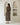 A woman stands with her back to the camera wearing a black and beige vertically striped midi dress with short flutter sleeves and a tie-neck detail. She is standing in a minimalist white room with arched recessed shelves containing decorative white ceramic vases.