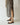 A person wearing black flat sandals with gold-tone toe loops and straps, paired with a black and beige vertically striped maxi dress, shown from the knees down in a minimalist indoor setting.